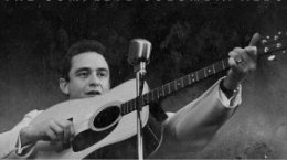 the person in Black lifts their electric guitar closer to the microphone.